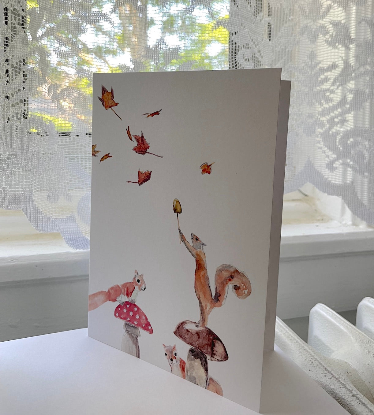 greeting card watercolor art, 3 suirrels  and mushrooms and automn leaves in the wind